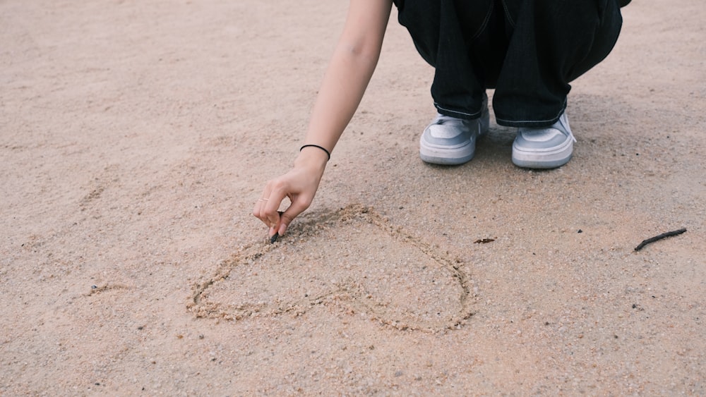 a person kneeling down and drawing a heart in the sand