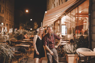A playful exchange of smiles between two people in a softly lit urban setting at night.