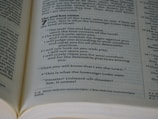 An open book showing a passage with biblical text. The page is filled with neatly aligned black text on white paper, with bold headings and numbers indicating chapters and verses.