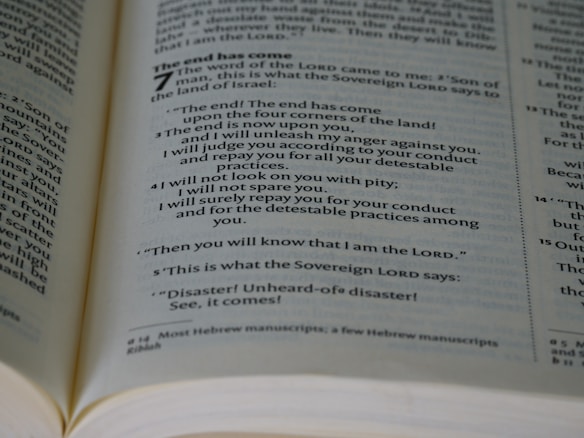 An open book showing a passage with biblical text. The page is filled with neatly aligned black text on white paper, with bold headings and numbers indicating chapters and verses.