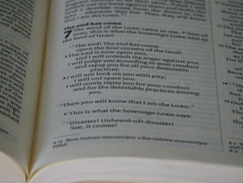 An open book showing a passage with biblical text. The page is filled with neatly aligned black text on white paper, with bold headings and numbers indicating chapters and verses.