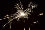 A bright sparkler with glowing sparks radiating outwards against a dark background.