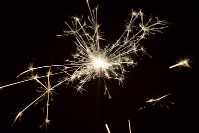 A bright sparkler with glowing sparks radiating outwards against a dark background.