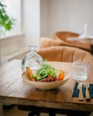 A rustic wooden table set with a fresh garden salad in a white ceramic bowl.