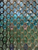 A pattern of hexagonal tiles in shades of blue and green, each with a textured, diamond-like interior design. The tiles are arranged in a regular, grid-like pattern, creating a visually striking and geometric display.