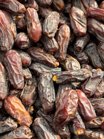 Close-up of fresh, glossy dates piled in a rustic wooden bowl.