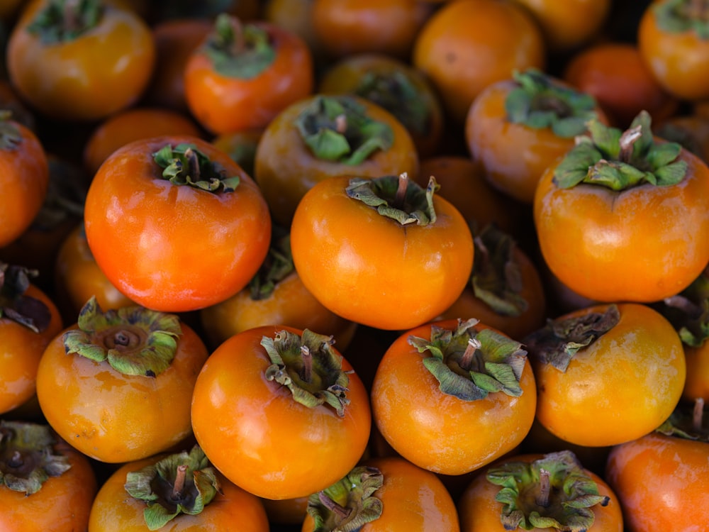 a pile of orange tomatoes with green leaves on them