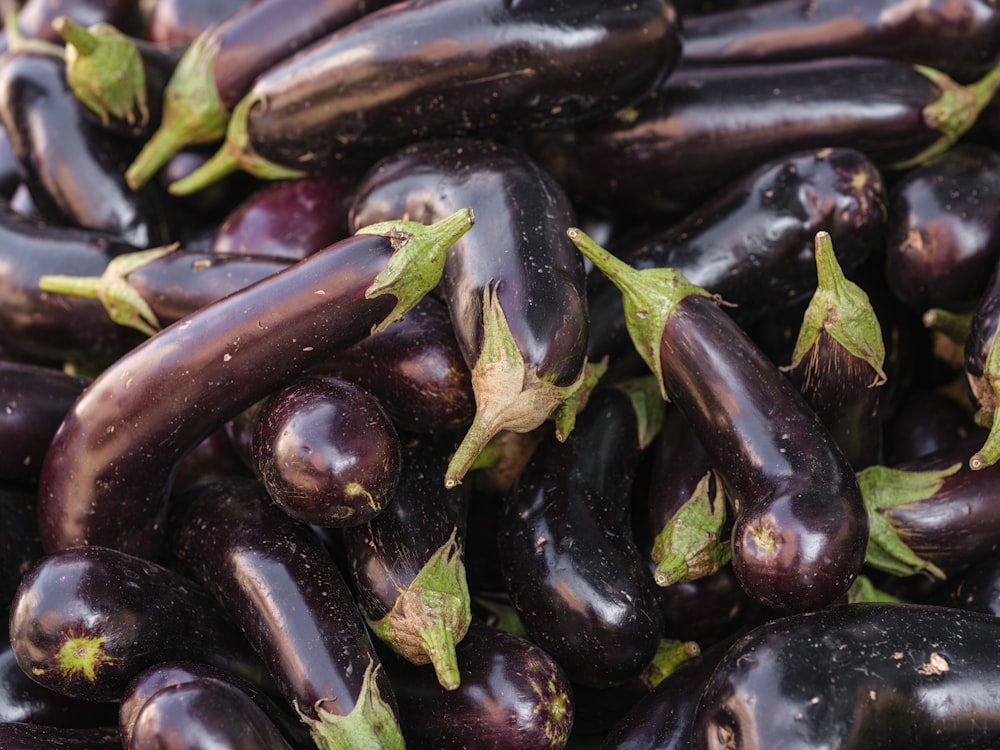 a pile of purple eggplant with green leaves