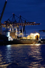 Port operations underway at night with a support vessel assisting in maneuvers.