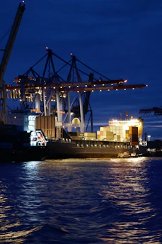 Port operations underway at night with a support vessel assisting in maneuvers.