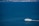 A white yacht is cruising through expansive blue waters with a distant coastal industrial area visible on the horizon.