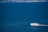 A white yacht is cruising through expansive blue waters with a distant coastal industrial area visible on the horizon.