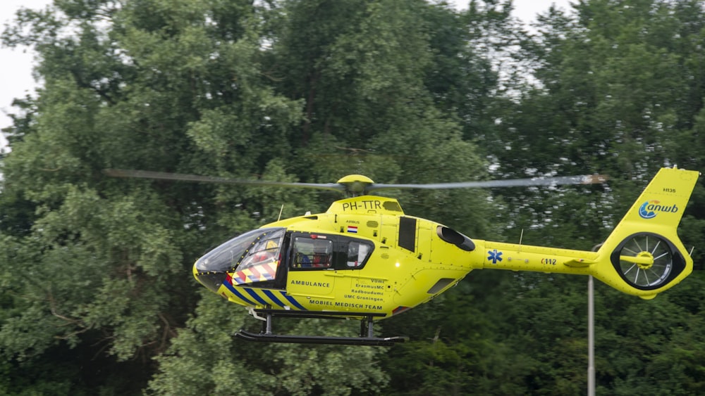 a yellow helicopter flying over a lush green forest