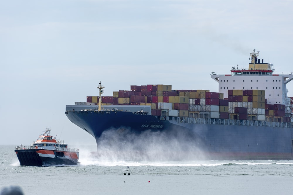 a large cargo ship in the ocean with a tug boat nearby