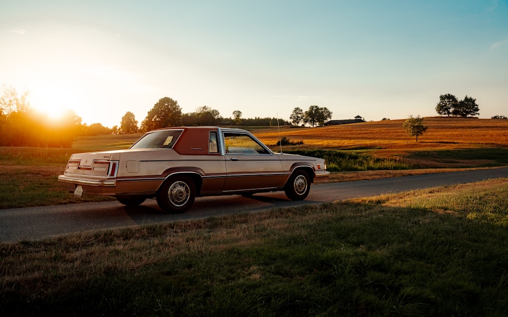 a brown car driving down a road next to a field