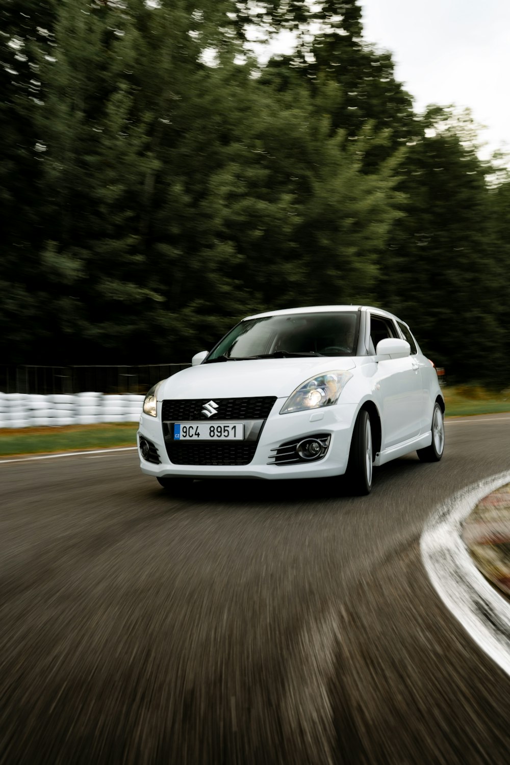 a white car driving down a road next to a forest