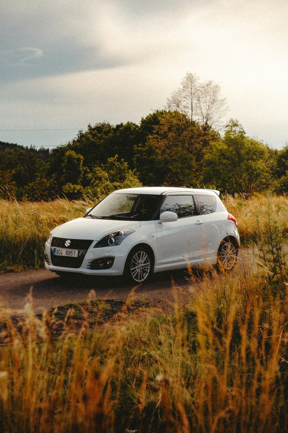 a small white car driving down a dirt road