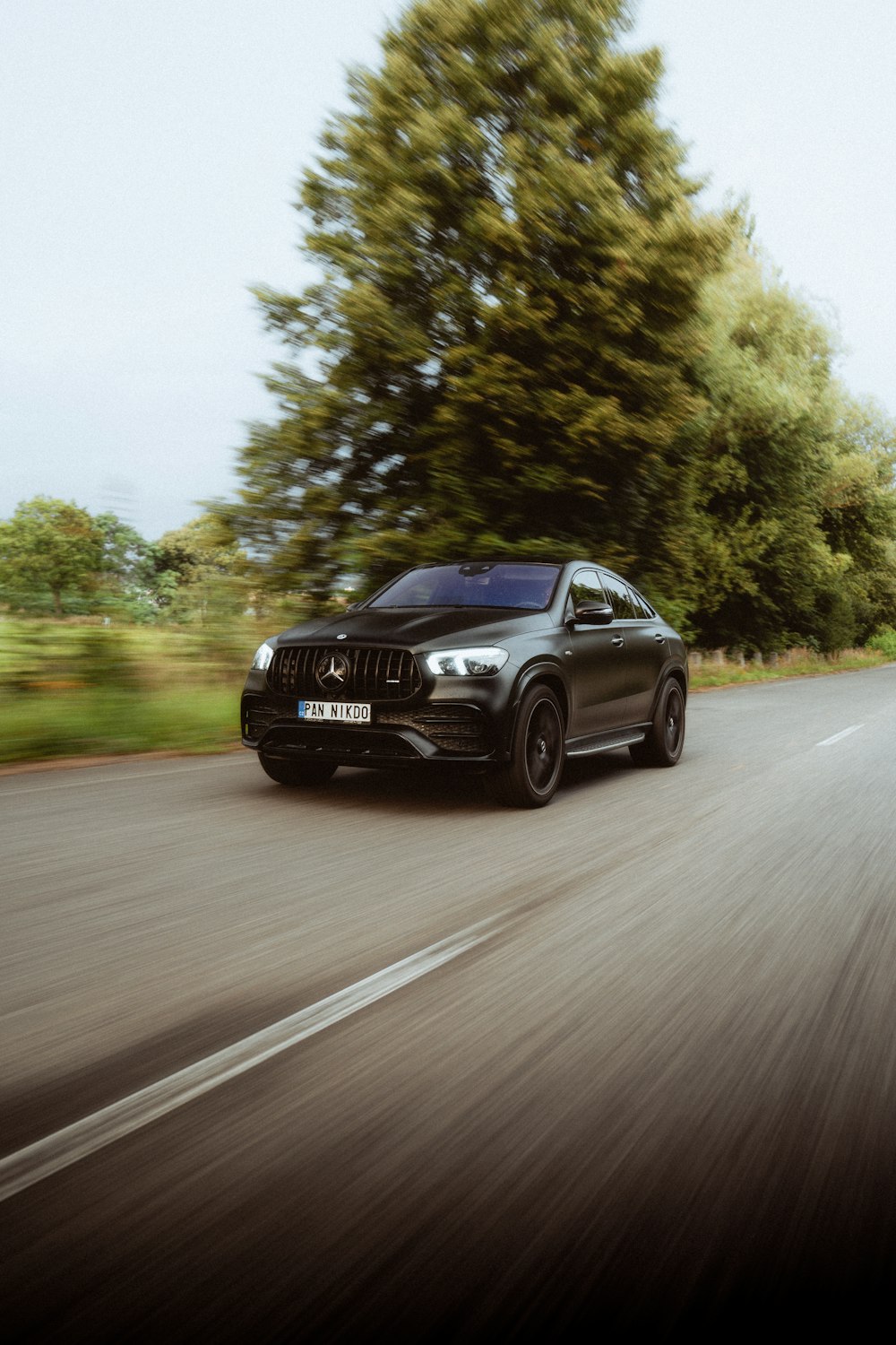 a black car driving down a road next to trees