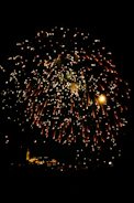 A vibrant burst of colorful fireworks illuminating a night sky over a city skyline.