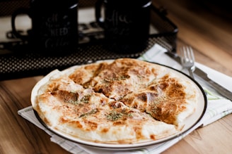 A golden-brown cheburek on a rustic wooden plate with a side of fresh herbs.