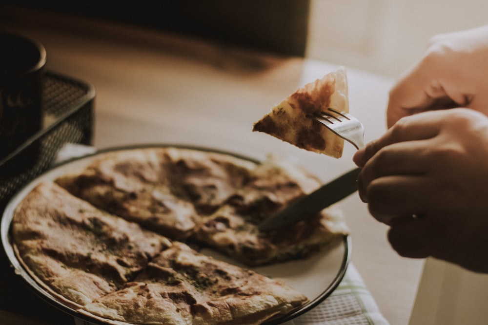 a person cutting a slice of pizza on a plate