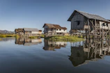 Exterior view of Na Can homestay with traditional stilt houses under blue sky.