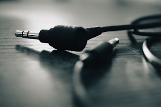 A close-up of two audio jack connectors lying on a wooden surface. The image has a shallow depth of field with one jack sharply in focus and the other blurred, creating a dramatic effect.