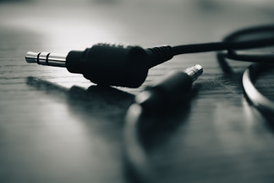 A close-up of two audio jack connectors lying on a wooden surface. The image has a shallow depth of field with one jack sharply in focus and the other blurred, creating a dramatic effect.