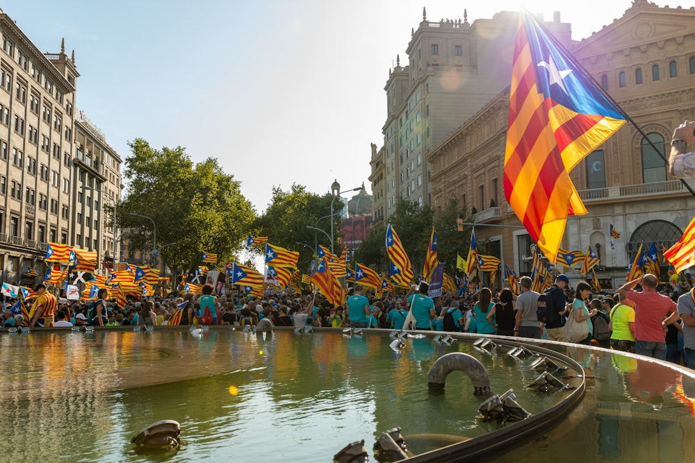 a crowd of people standing around a fountain with flags