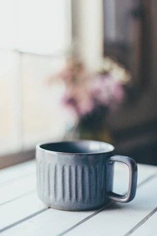 Close-up of a delicate mug with an encouraging quote, resting on a light wooden table beside a small bouquet of fresh flowers.