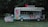 A coffee truck situated in a park-like setting surrounded by lush greenery. The truck features a sign that reads 'K COFFEE' with images of various drinks displayed on its side. Bright and vivid advertisements for ice cream and beverages are visible on the grass next to the truck, promoting colorful and appetizing drinks. The overall scene is serene and inviting, with the food truck standing out against the natural background.