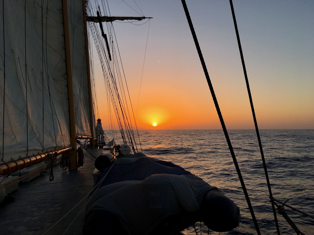 the sun is setting over the ocean on a sailboat