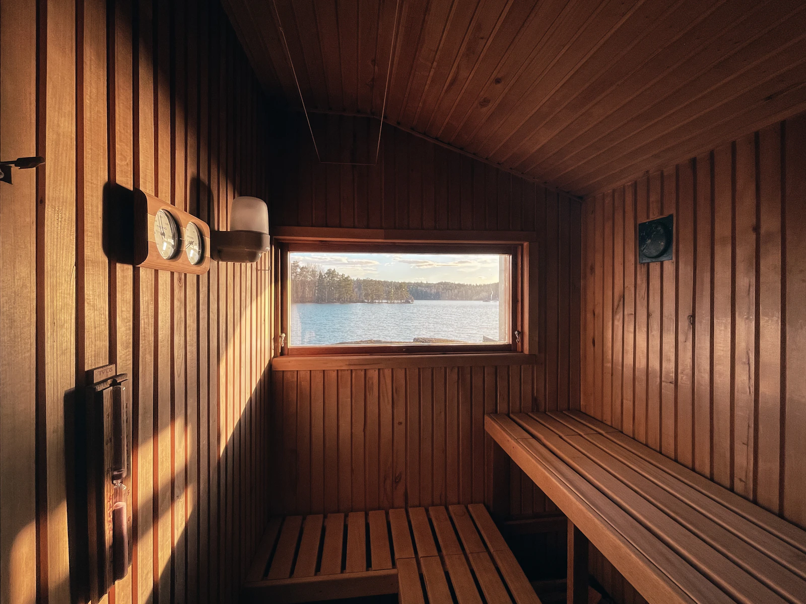 A warm cedar sauna at golden hour, its window open to a calm lake