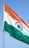 A tricolor flag with horizontal stripes of saffron at the top, white in the middle featuring a blue Ashoka Chakra, and green at the bottom, set against a clear blue sky.