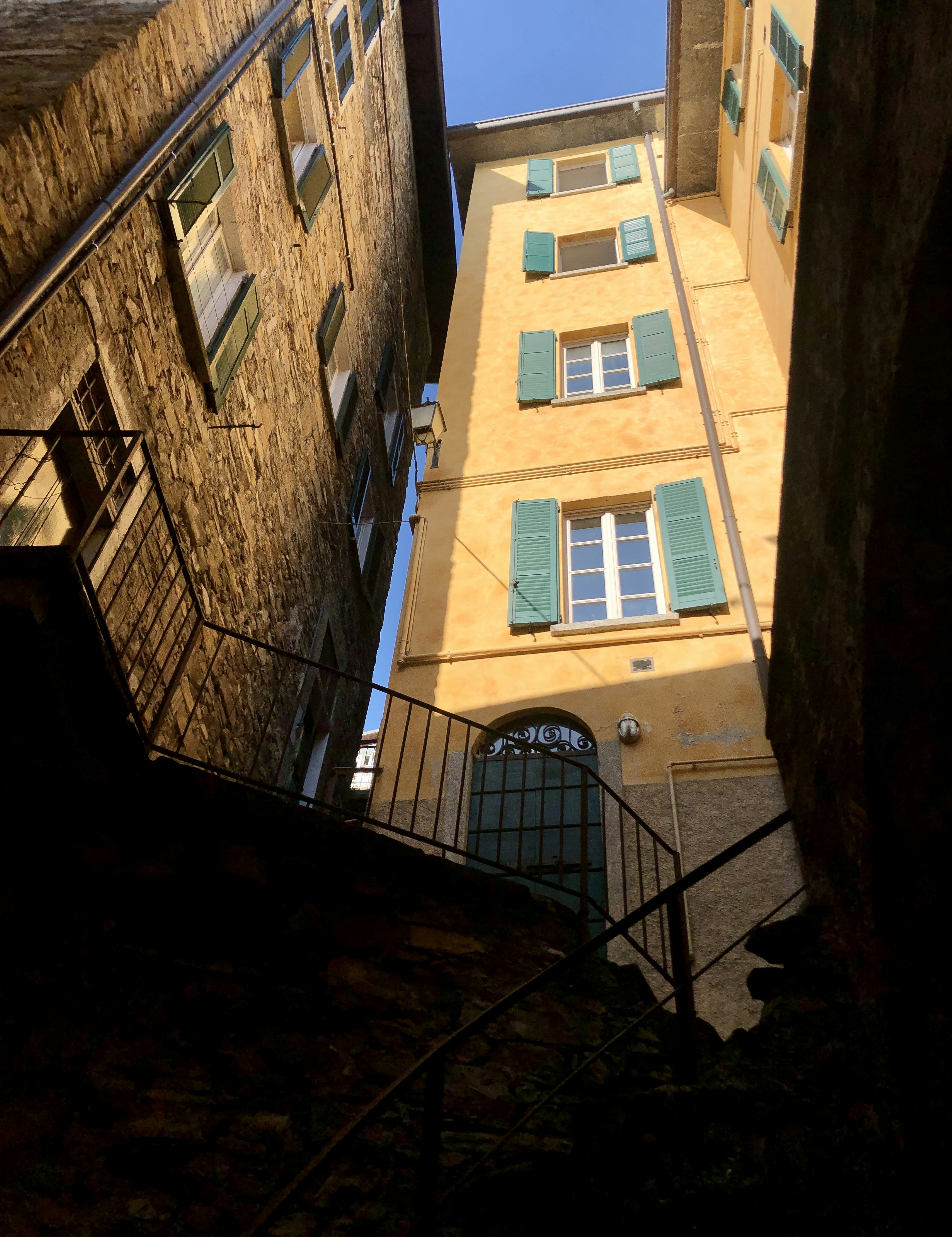 a narrow alley way with a yellow building and green shutters