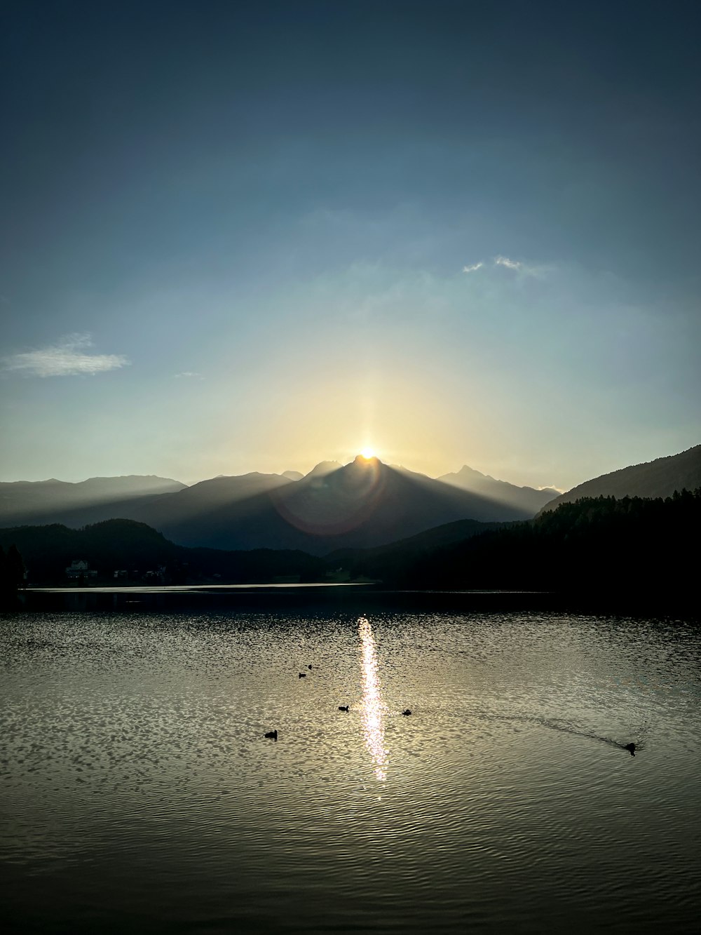 山々を背景にした湖に太陽が沈む