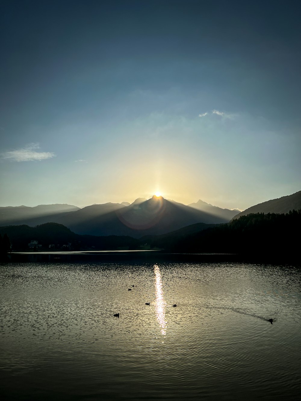 the sun is setting over a lake with mountains in the background