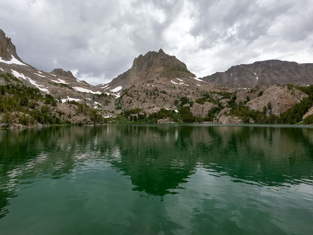 a body of water surrounded by mountains under a cloudy sky