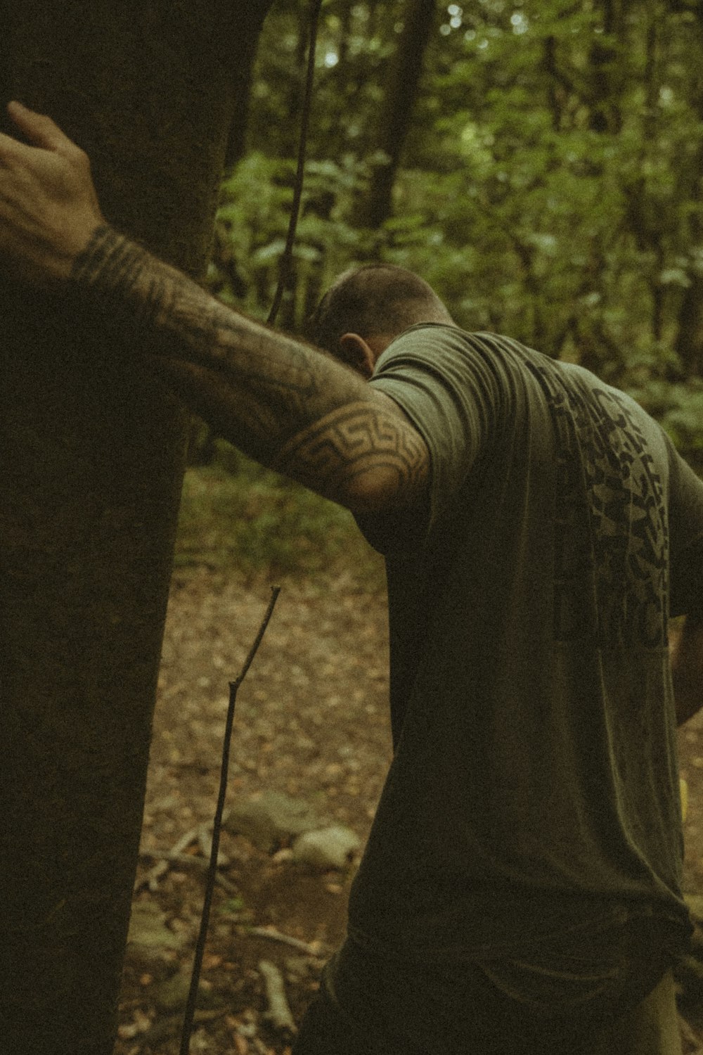 a man with a tattoo on his arm standing next to a tree