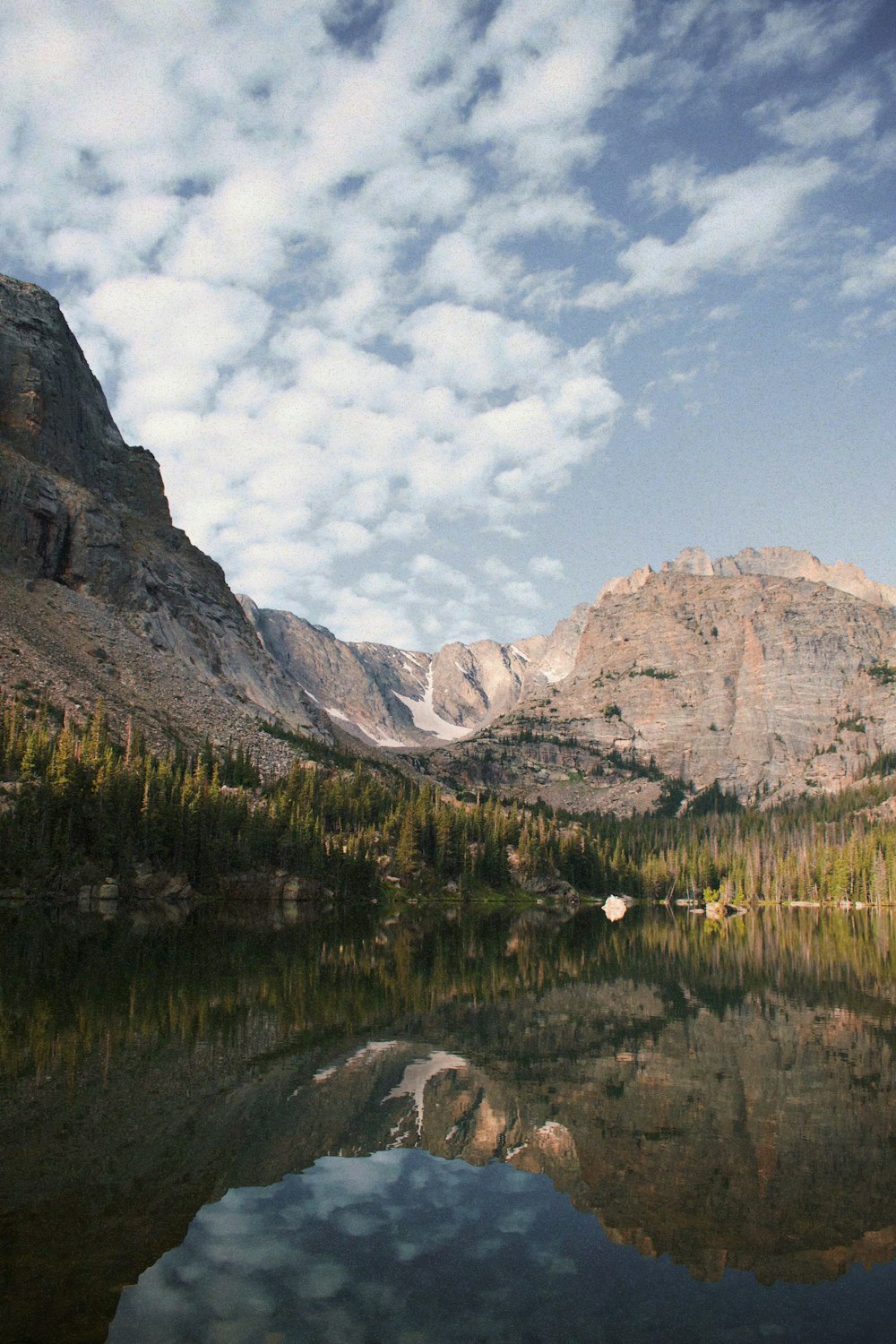 a lake surrounded by mountains and trees under a cloudy sky