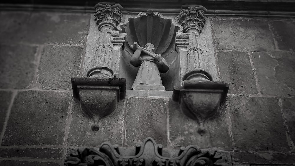a black and white photo of a statue on the side of a building
