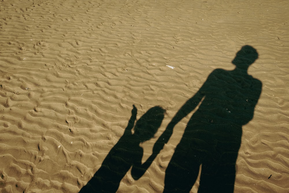 uma sombra de um homem e uma criança em uma praia