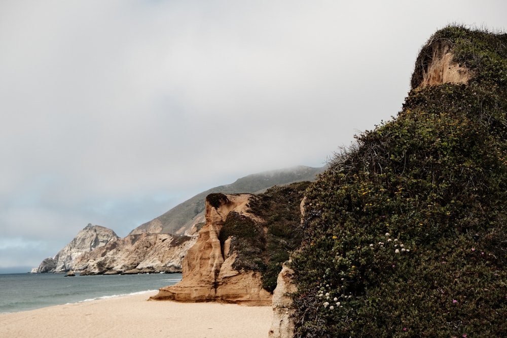 a sandy beach next to the ocean with a mountain in the background