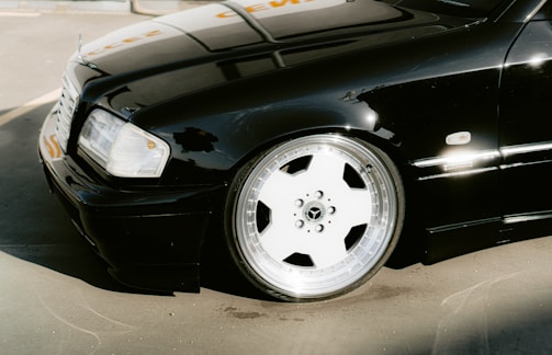 A black luxury sedan is parked, showcasing a shiny, polished chrome wheel with a five-spoke design. The vehicle's exterior is clean and reflects light, indicating a well-maintained condition.