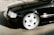 A black luxury sedan is parked, showcasing a shiny, polished chrome wheel with a five-spoke design. The vehicle's exterior is clean and reflects light, indicating a well-maintained condition.