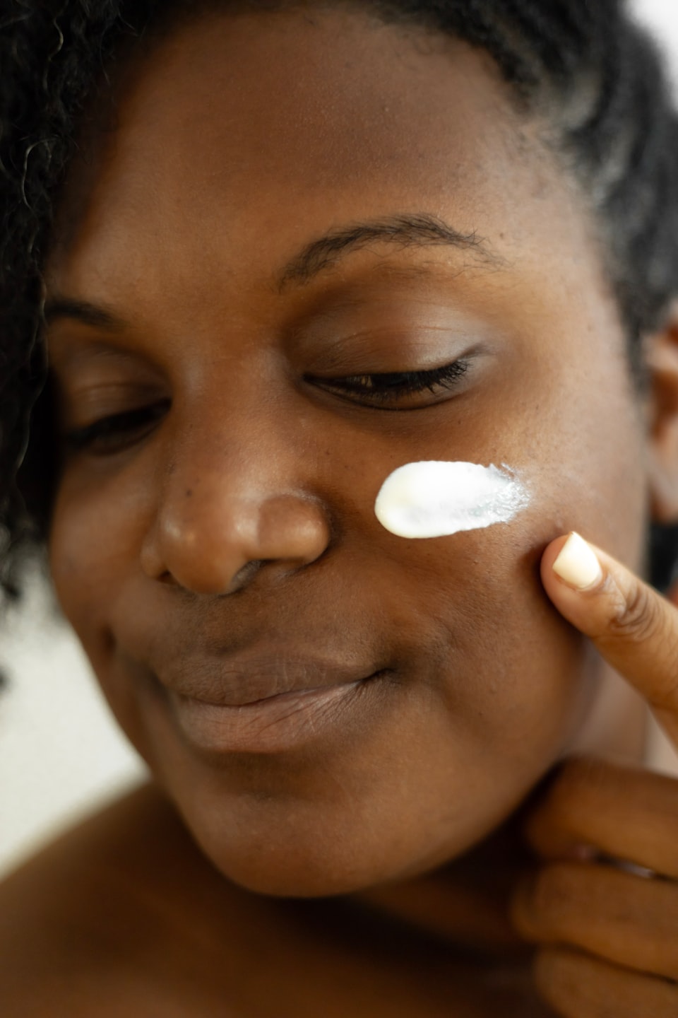 lady with dark skin pointing her finger to a dollop of facial cream on her check on a white background