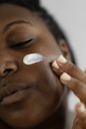 A close-up of hands applying a cream on a glowing face.