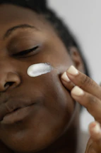 A serene close-up of a woman gently applying cream to her glowing skin.