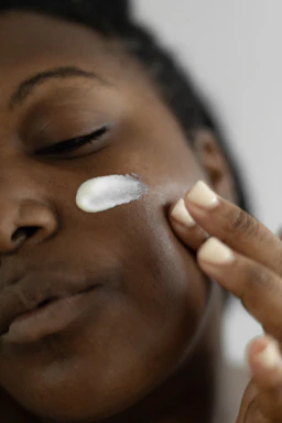 A serene close-up of a woman gently applying cream to her glowing skin.