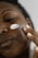 A smiling woman with glowing skin gently applying cream to her cheek in a bright, clean bathroom.